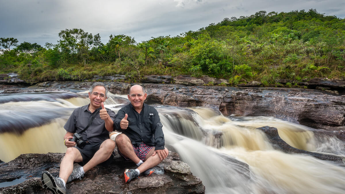 Dos fotógrafos mexicanos en Caño Cristales, sentados sobre una roca a orillas de un río con cascadas